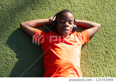 Listening to music, boy in orange shirt relaxing on grass outdoors 125353999