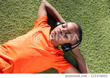 Listening to music, boy relaxing on grass with headphones, enjoying leisure time Listening to music, boy relaxing on grass with headphones, enjoying leisure time 125354003