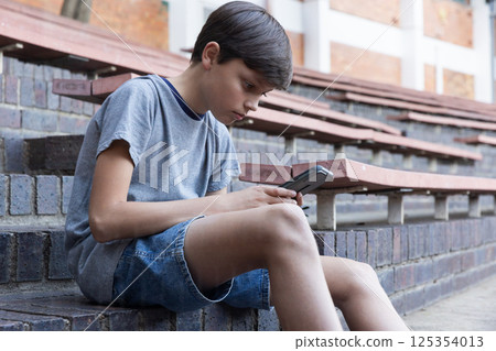 Sitting on bleachers, boy using smartphone at school during break time 125354013