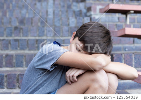 Sitting on steps, boy resting head on arms, feeling sad at school Sitting on steps, boy resting head on arms, feeling sad at school 125354019