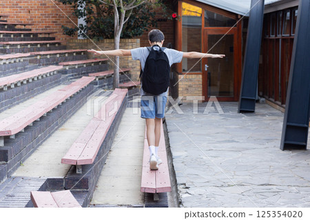 Balancing on bench, boy with backpack enjoying outdoor activity at school Balancing on bench, boy with backpack enjoying outdoor activity at school 125354020