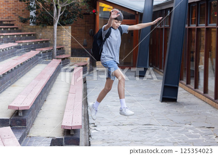 Jumping down steps, boy with backpack enjoying courtyard at school 125354023