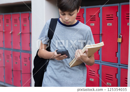 At school, boy holding books and using smartphone near lockers At school, boy holding books and using smartphone near lockers 125354035