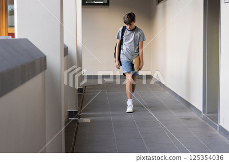 Walking in school hallway, boy carrying book and backpack, looking down, copy space Walking in school hallway, boy carrying book and backpack, looking down, copy space 125354036