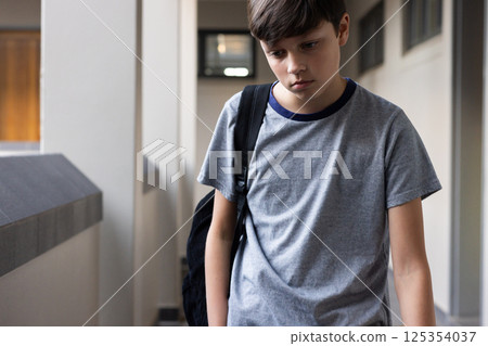 Walking in school hallway, boy with backpack looking down, feeling sad 125354037