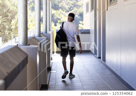 Walking down school hallway, boy carrying backpack and wearing striped shirt 125354062
