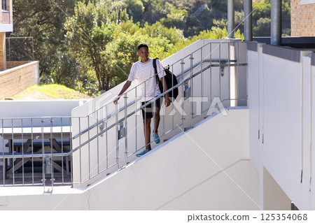 Walking up stairs, student carrying backpack and holding railing at school, copy space 125354068