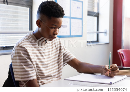 In school, boy writing in notebook at desk, concentrating on work 125354074