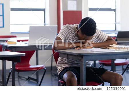 In school, boy resting head on desk in classroom, looking tired 125354091