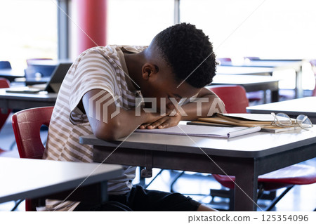 Sleeping on desk, student in school classroom with books and glasses nearby 125354096