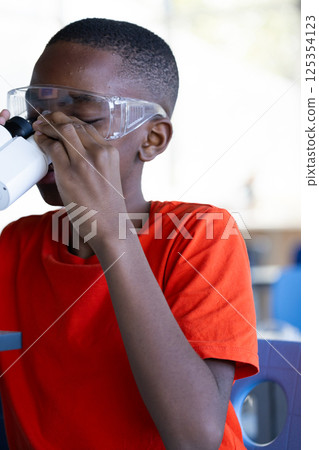 Using microscope, boy in school wearing safety goggles, focusing on experiment 125354123