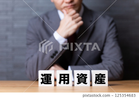 A middle-aged male businessman wearing a suit and a block of investment assets 125354683