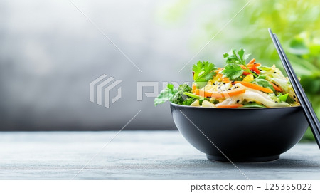 Fresh vegetable stir fry in black bowl on rustic table with chopsticks 125355022