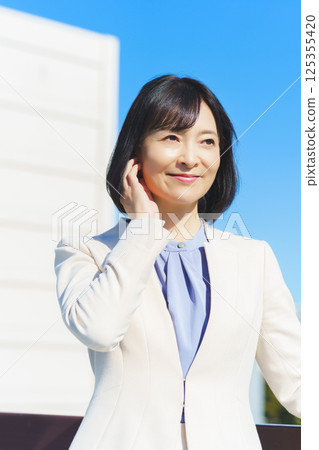 A middle-aged career woman in a white suit under a blue sky 125355420