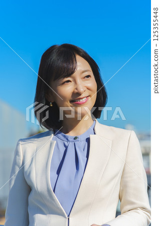 A middle-aged career woman in a white suit under a blue sky 125355448