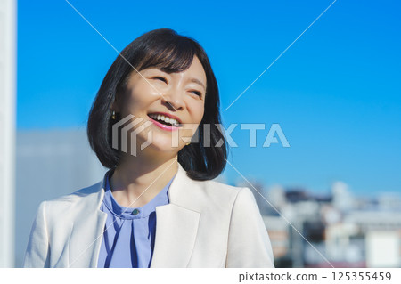 A middle-aged career woman in a white suit under a blue sky 125355459