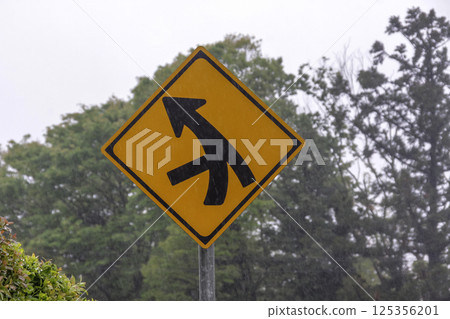 A warning sign for merging traffic, a little hazy due to rain 125356201