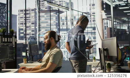 Managers evaluating work done by computer scientists in workspace doing software debugging. Management executives walking in office with tablet, checking code fixed by employees, camera B 125356276
