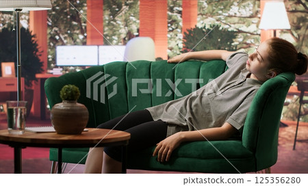Therapy session with a teenage girl laying on couch discussing trauma and hormonal shifts. Psychotherapist supporting her emotional development, guiding through depression and anxiety. Camera A. 125356280