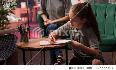 During a therapy session, an adolescent girl practices drawing to help with behavioral therapy and emotional regulation. The therapist and mother provide support for her mental wellbeing. Camera A. During a therapy session, an adolescent girl practices drawing to help with behavioral therapy and emotional regulation. The therapist and mother provide support for her mental wellbeing. Camera A. 125356304