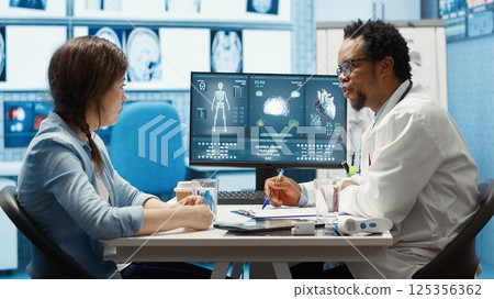 General practitioner presenting the diagnostic report at checkup with patient, discussing about treatment plan. Medic showing x ray imaging and scans on computer, medical results. Camera A. 125356362