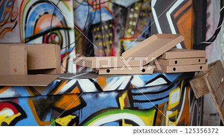 Graffiti spraying cans and empty pizza boxes in derelict building, concept of alternative lifestyle. Dolly in shot of base of operations in city slums used by criminals to commit illegal activities 125356372