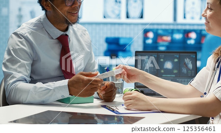 Medic recommending supplements and painkillers on medical insurance, writing a prescription document with instructions and the right dosage of medication. Modern healthcare services. Camera A. 125356461