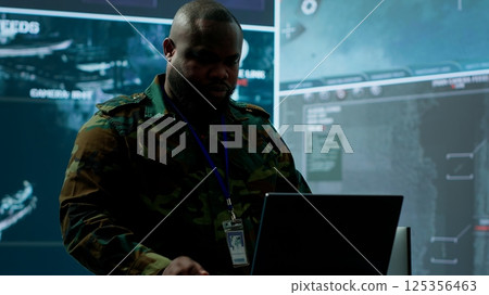 Military expert in a control center uses advanced technology and gear to gather intelligence from satellite imagery and surveillance systems. Using laptop to communicate information. Camera A. Military expert in a control center uses advanced technology and gear to gather intelligence from satellite imagery and surveillance systems. Using laptop to communicate information. Camera A. 125356463
