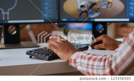 Male engineer designs 3D prototypes in a modern industrial interface using CAD software. Specialist creating gears and machinery tools via 3D modeling, technical expertise. Camera B. 125356503