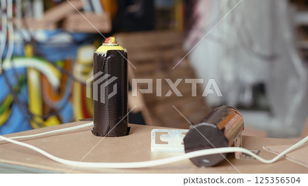 Close up of spray cans in colorful basement filled with graffiti art used as hanging place by skaters. Focus on paint cans in artsy abandoned building filled with paint artworks by teenagers 125356504