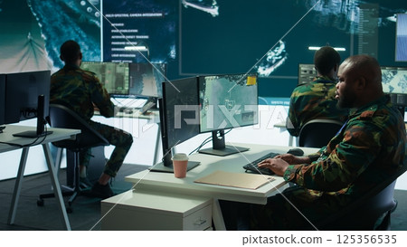 Army intelligence specialists using advanced computer systems and satellite data to enhance national security, critical information. Soldiers planning for mission in high tech control room. Camera B. 125356535