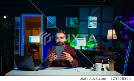 Tech expert presenting tablet in entry level low budget price range to interested viewers, filming in studio. Viral content creator reviewing digital device in front of internet audience, camera B 125356593