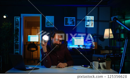 Entertainer using light bulb to create atmospheric mood while entertaining audience. Disheveled man in apartment using light to create spooky vibe, pretending to be electrocuted, camera B Entertainer using light bulb to create atmospheric mood while entertaining audience. Disheveled man in apartment using light to create spooky vibe, pretending to be electrocuted, camera B 125356628