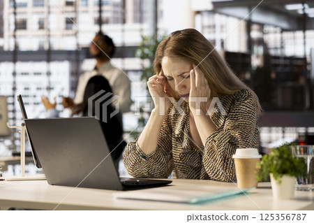 Stressed businesswoman faces a migraine from corporate pressure, feeling overworked and frustrated. Woman feeling overwhelmed by deadlines and struggles with burnout, emotional strain. 125356787