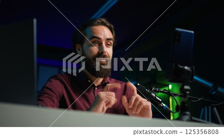 ASMR content creator using quality mic and cellphone on tripod to do anti stress video, using whispering voice, close up. Man using professional microphone to induce sleepiness to viewers, camera B ASMR content creator using quality mic and cellphone on tripod to do anti stress video, using whispering voice, close up. Man using professional microphone to induce sleepiness to viewers, camera B 125356808