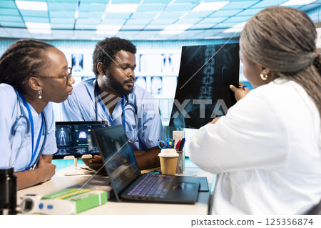 Group of doctor and junior nurses specialists in scrubs analyzing results, emphasizing teamwork and professional training at private clinic. African american medical staff doing research. Group of doctor and junior nurses specialists in scrubs analyzing results, emphasizing teamwork and professional training at private clinic. African american medical staff doing research. 125356874