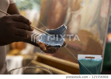 Skilled painter wiping the brush on denim fabric to clean the colors, applying a different dye shade on canvas. Talented man working hard on his new artistic painting. Close up. 125356908