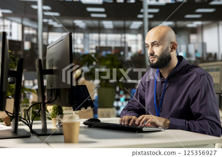 Confident male manager multitasking at the office to handle administrative tasks on the workstation, business tasks. Young man reviewing documents and meeting project deadlines. 125356927