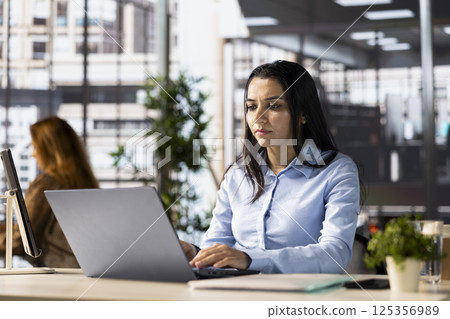 Indian businesswoman reviews financial plans using online tools for decision making and strategy planning. Worker managing enterprise objectives and business operations, focused on success. Indian businesswoman reviews financial plans using online tools for decision making and strategy planning. Worker managing enterprise objectives and business operations, focused on success. 125356989