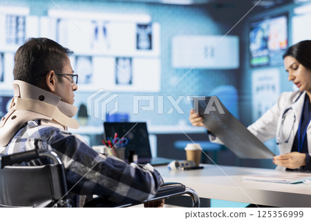 Indian medic reviewing x ray imaging test findings to patient with disability, recommending physiotherapy and professional wellness exercises. Female specialist assisting man with neck collar. Indian medic reviewing x ray imaging test findings to patient with disability, recommending physiotherapy and professional wellness exercises. Female specialist assisting man with neck collar. 125356999