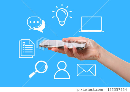 User interacts with mobile device amidst icons conveying communication and technology 125357334