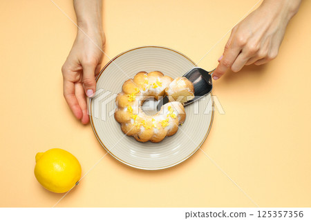Lemon cake on plate, lemon and female hands on beige background, top view 125357356