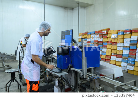 Worker using a digital tablet to monitor machinery in a food processing facility Worker using a digital tablet to monitor machinery in a food processing facility 125357404