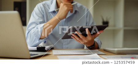 Businessperson analyzing data on digital tablet while seated at a desk Businessperson analyzing data on digital tablet while seated at a desk 125357459