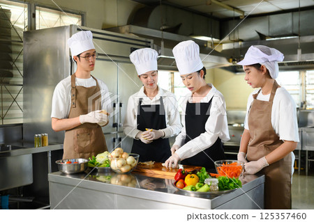 Group of young chefs in training focused on cutting vegetables during a cooking class Group of young chefs in training focused on cutting vegetables during a cooking class 125357460