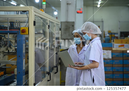 Factory workers overseeing automated packaging equipment in canned fish processing Factory workers overseeing automated packaging equipment in canned fish processing 125357477