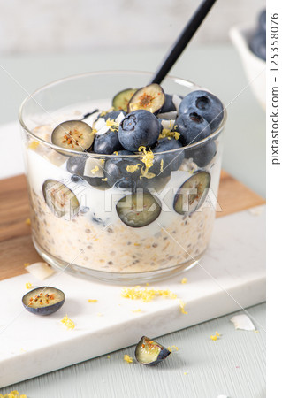 Healthy blueberry Lemon Overnight Oats topped with blueberries, lemon zest and coconut shavings on a light blue wooden counter. Concept for healthy eating and nutrition. Healthy blueberry Lemon Overnight Oats topped with blueberries, lemon zest and coconut shavings on a light blue wooden counter. Concept for healthy eating and nutrition. 125358076
