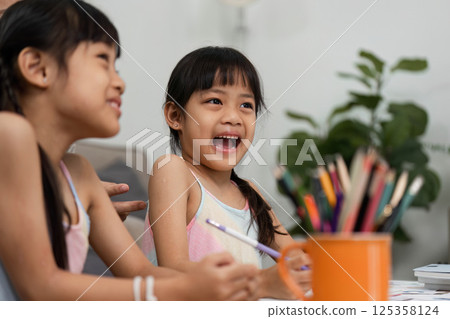 Back to School Fun and Creativity. Two girls enjoying art activities together, sharing laughter and creativity in a cozy home environment. 125358124