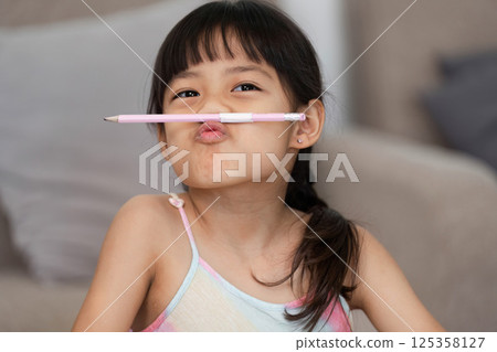 Silly Moments and Imagination. A girl making funny faces with a pencil, showcasing her playful spirit during art time. Silly Moments and Imagination. A girl making funny faces with a pencil, showcasing her playful spirit during art time. 125358127