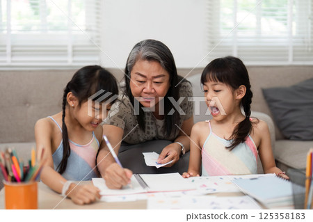 Learning and Family Bonding. A grandmother engaging with her grandchildren in a creative drawing session at home. 125358183